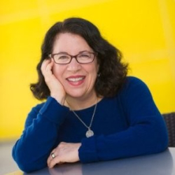 Photo of Laura Epstein smiling in blue sweater against yellow background